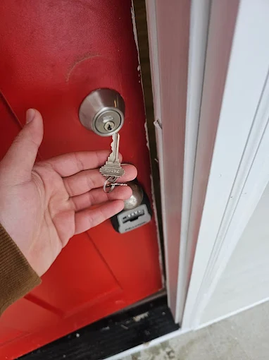 New house keys handed over at a red front door beside a realtor lockbox