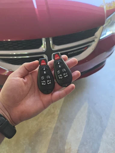 Two replacement Dodge Grand Caravan key fobs in front of a red minivan
